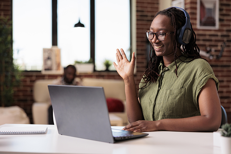 Student with wireless headphones in video conference waving hello at colleagues